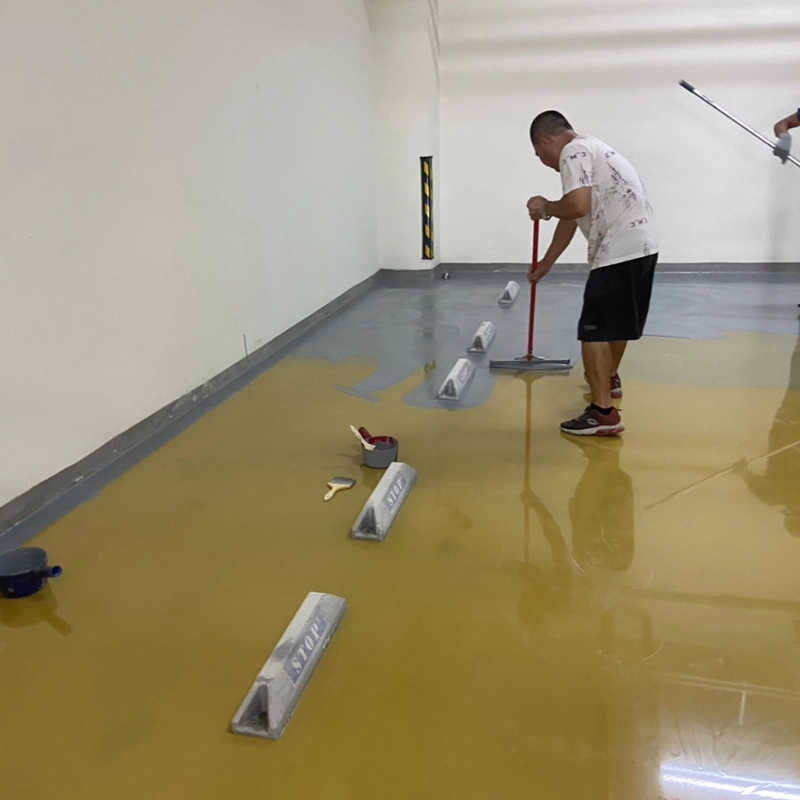 A worker applying grey self-leveling epoxy over a yellow base in a parking area.