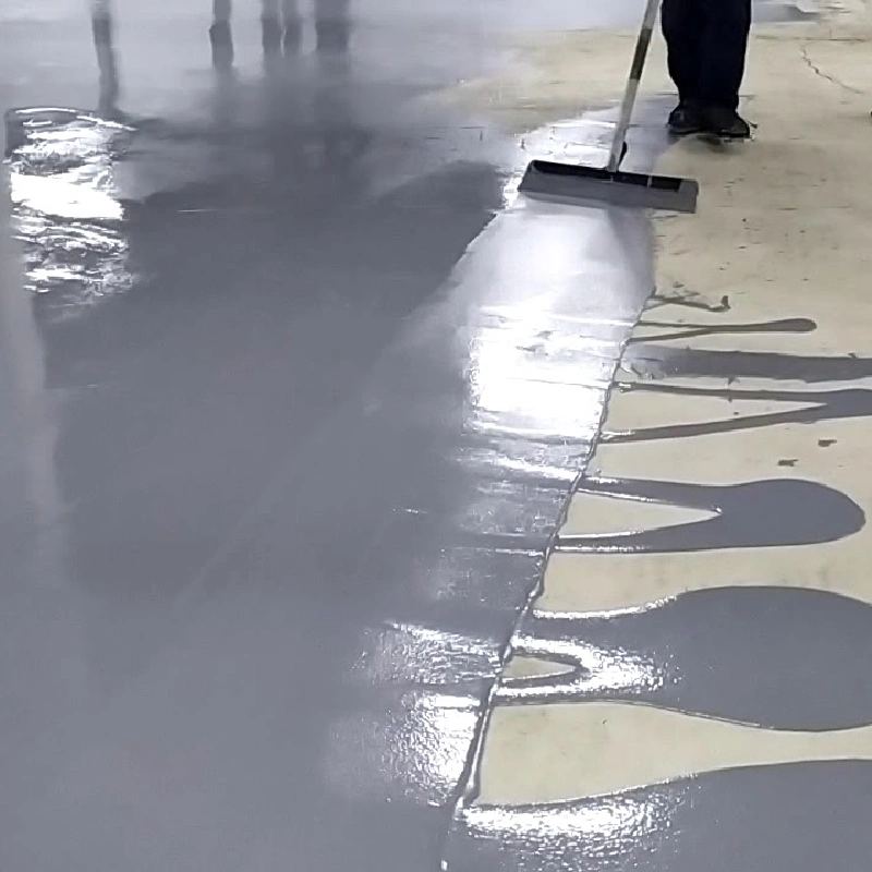 Spreading a thick layer of grey self-leveling epoxy over a concrete floor.