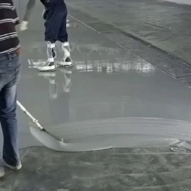 worker in spiked shoes spreading grey self-leveling epoxy on a large floor.