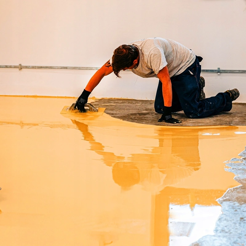 worker using a notched trowel to spread yellow self-leveling epoxy resin.